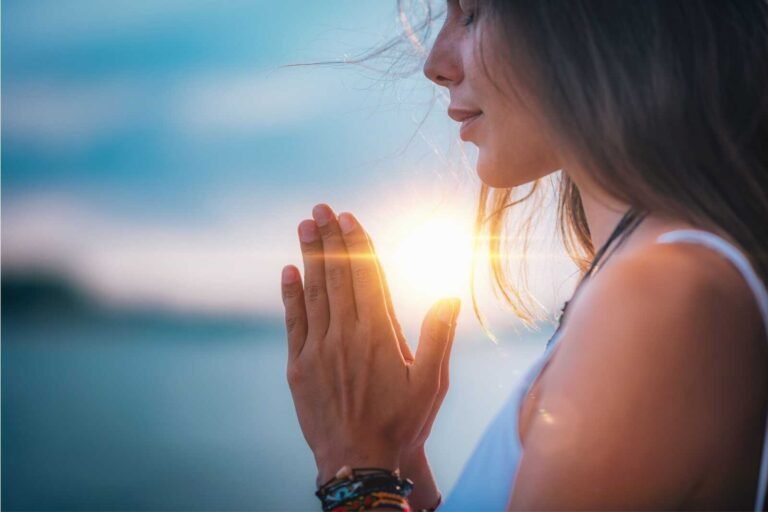 Woman praying at sunrise with hands clasped, symbolizing hope and faith during a Christian fertility prayer.