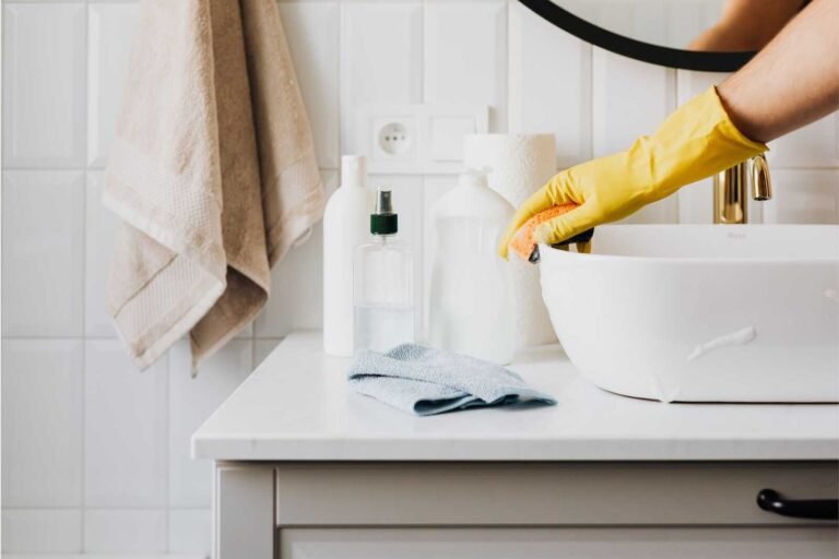 Cleaning a bathroom sink with a sponge, showing homemaking skills every wife should know.