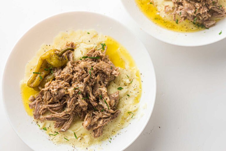 Slow cooker Mississippi Pork Roast over mashed potatoes with pepperoncini peppers