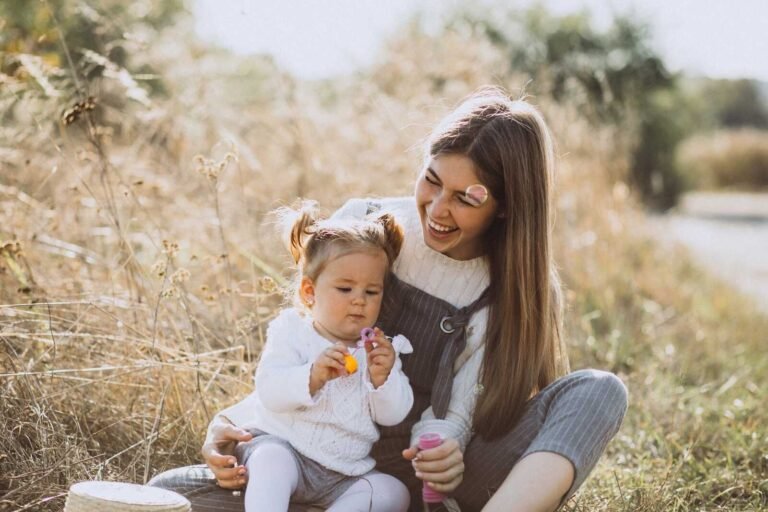 Mom and baby sitting together during a warm outdoor mom and baby photoshoot in a grassy field.