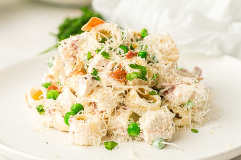 Creamy chicken pasta salad with bacon, peas, Parmesan cheese, and parsley served on a white plate.