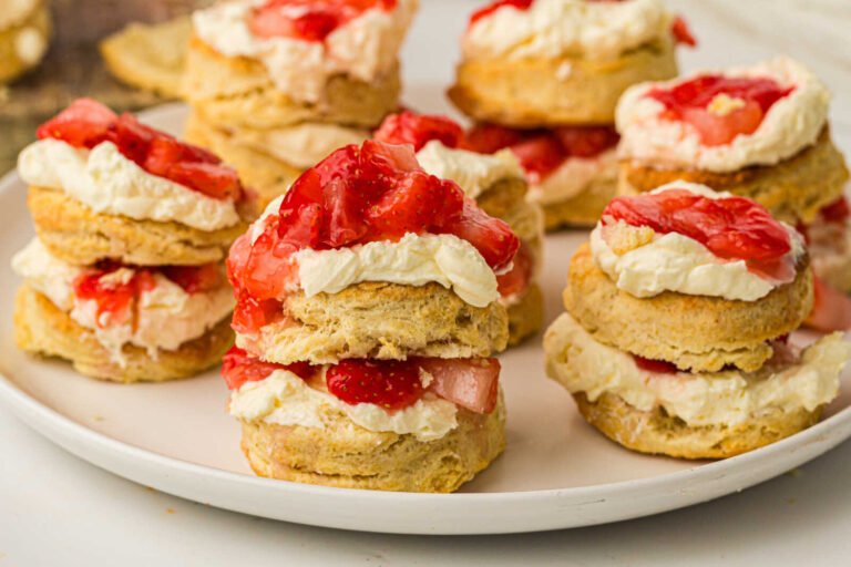 Homemade strawberry shortcakes topped with whipped cream and fresh strawberries on a serving platter.