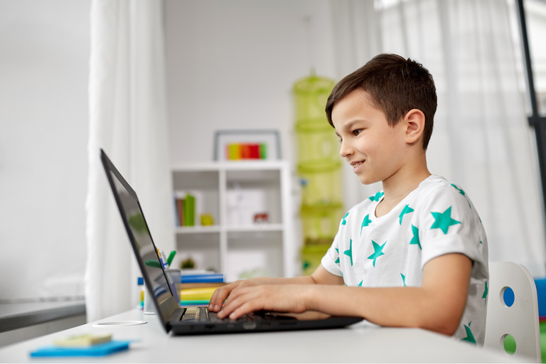 Young boy using a laptop at home to illustrate how to keep kids safe online.