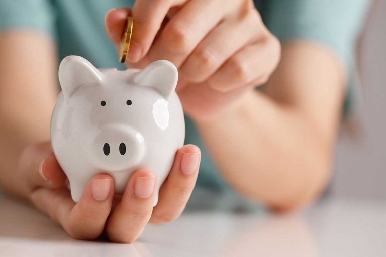 Person placing a coin into a piggy bank to build a college fund.