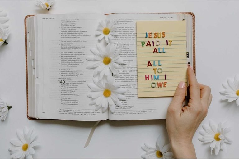 NLT Journaling Bible open with daisies and a Christian message reading “Jesus Paid It All.”