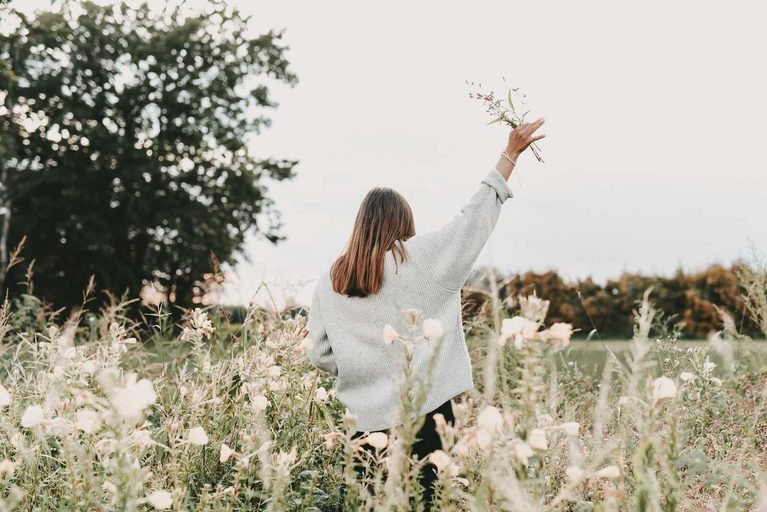 Woman holding wildflowers in a field representing Bible Quotes for Self Love and finding confidence through faith.